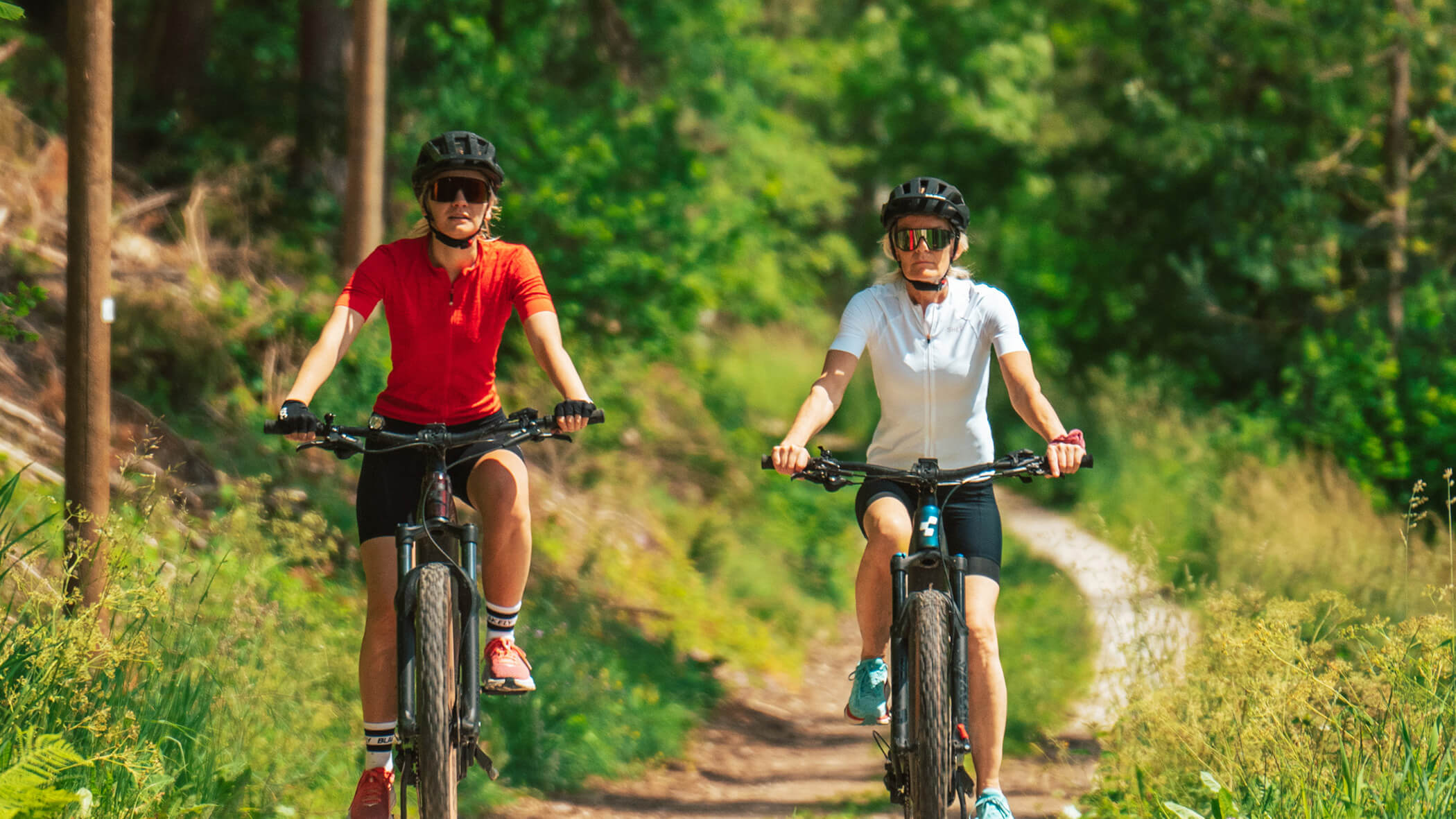 Zwei Frauen beim Radfahren zwischen Bäumen und Wiesen - Oberplunerhof