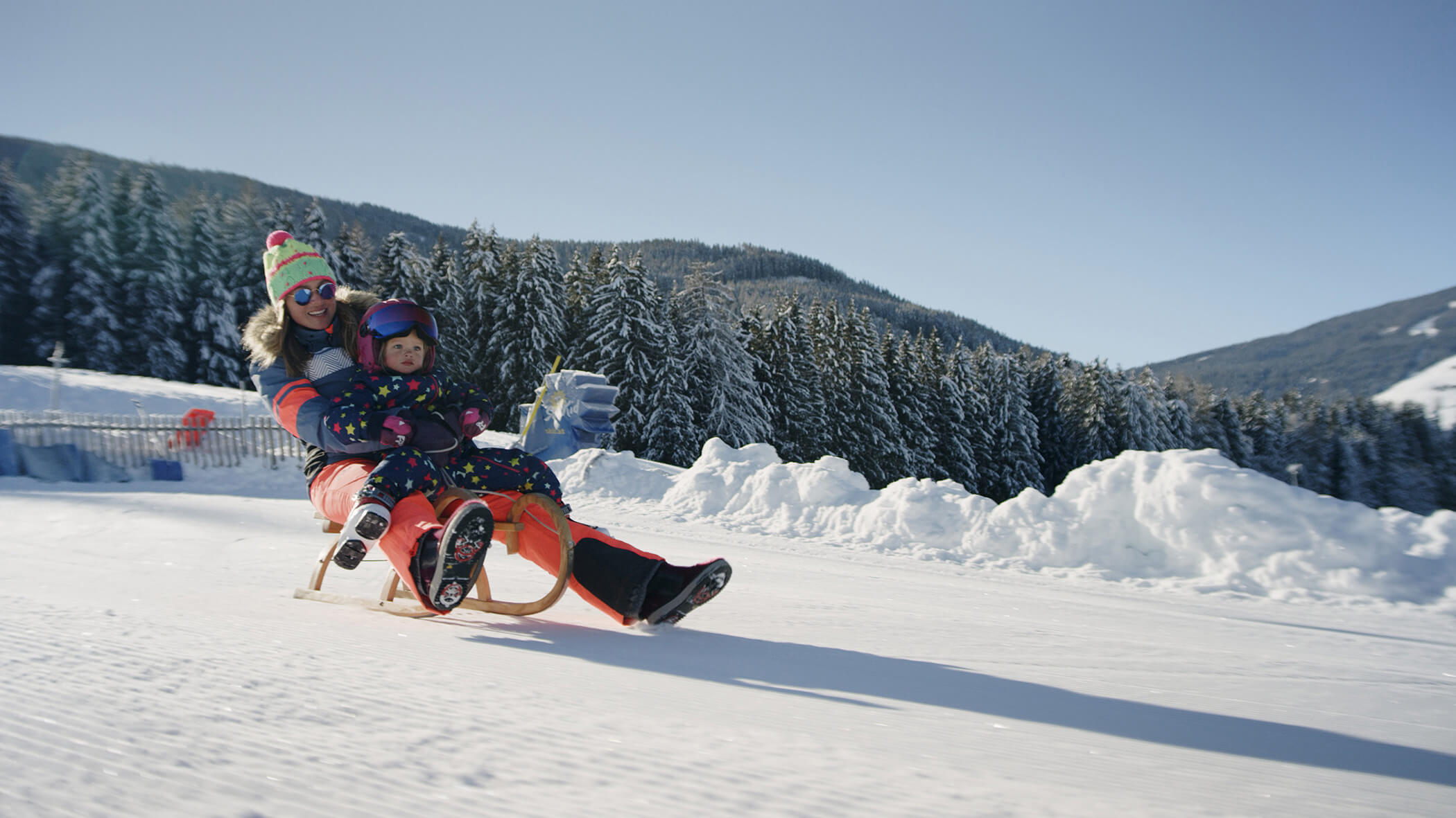 Frau rodelt mit ihrer Tochter die Skipiste hinunter - Oberplunerhof