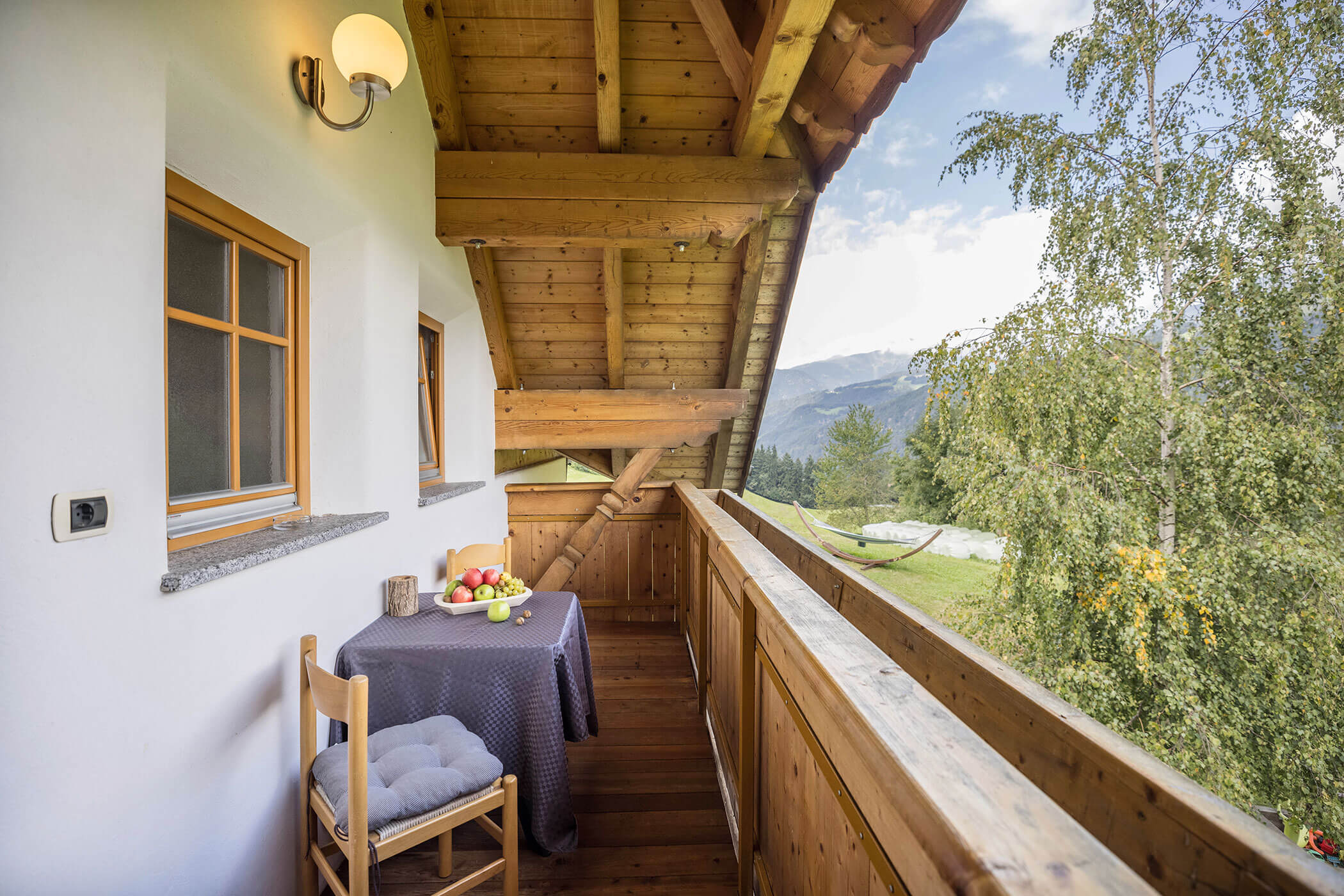 The balcony of Apartment Brunico with two chairs and a table with a view of the mountains and trees - Oberplunerhof