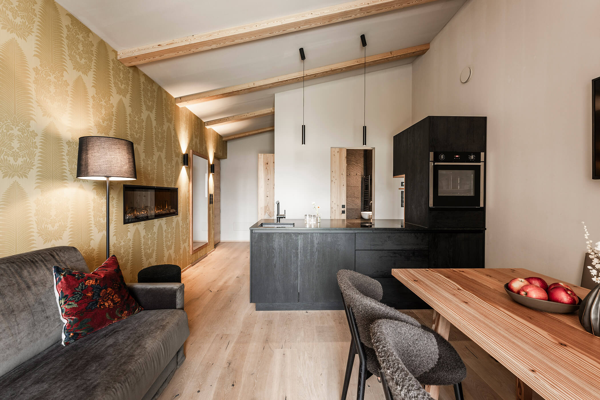 Kitchen-living room with dark kitchenette, dining table and gray sofa - Oberplunerhof