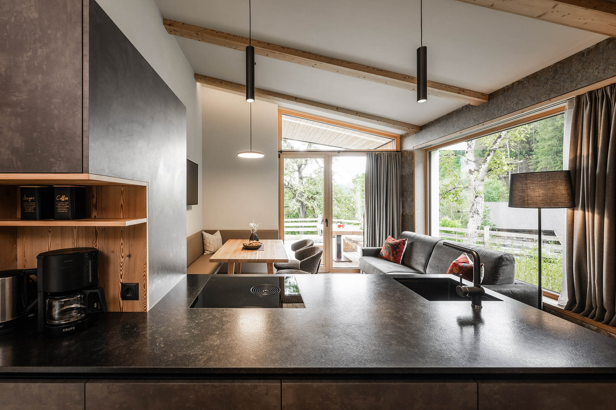 Kitchen-living room in Chalet Woods with dark kitchenette, wooden table and sofa - Oberplunerhof
