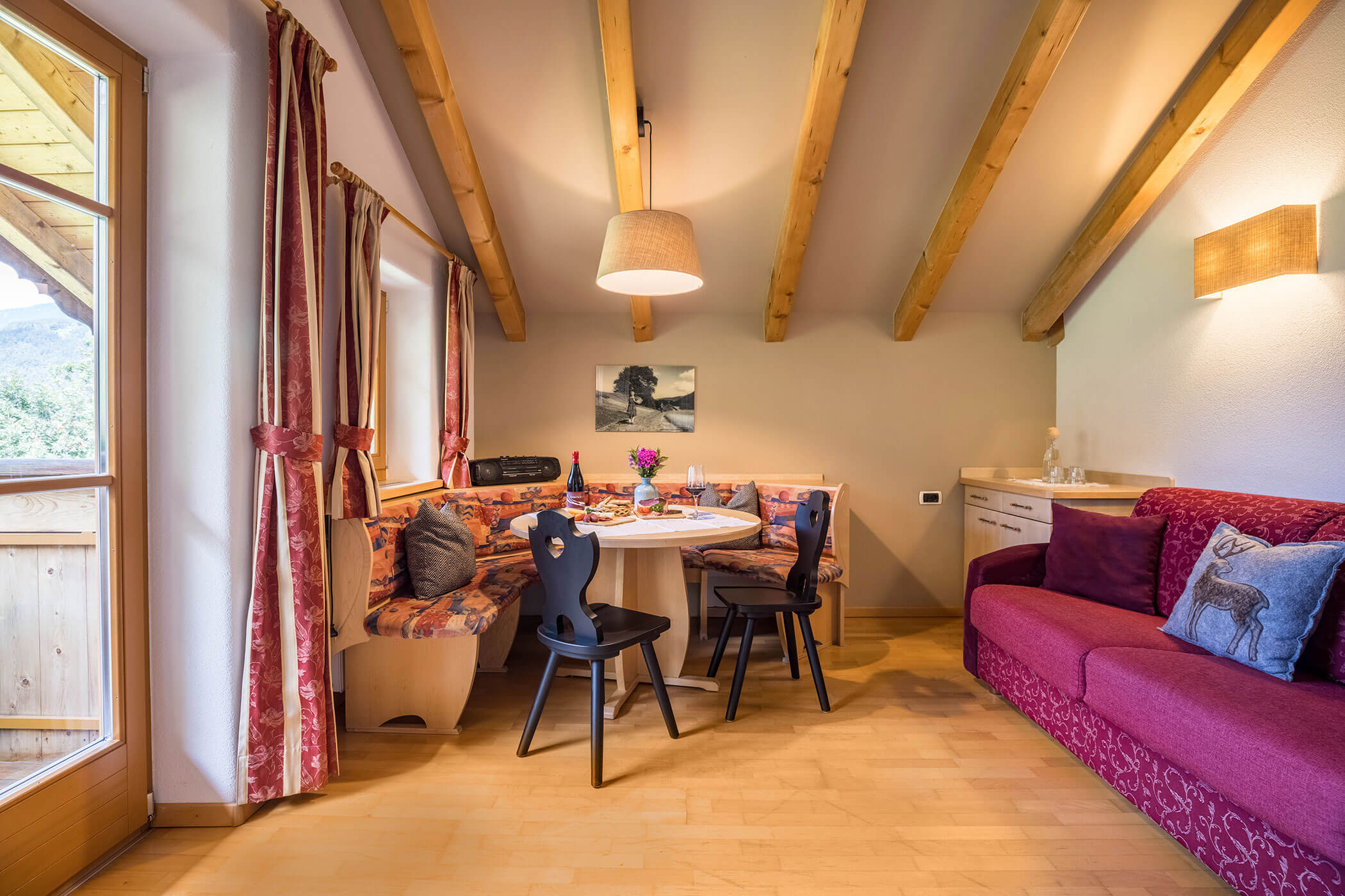 Living-dining room with red sofa, corner bench, table and two chairs - Oberplunerhof