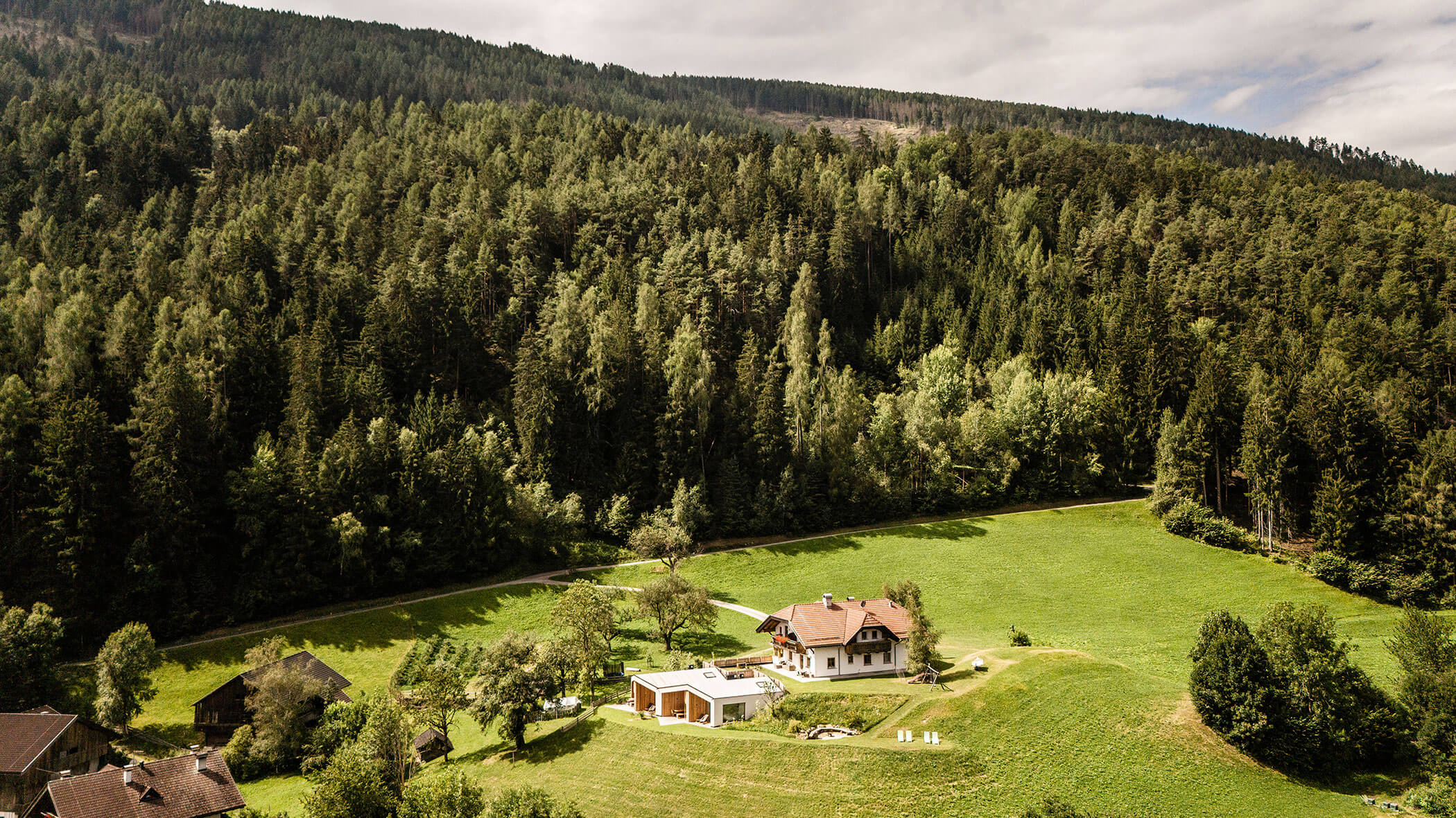 The Oberplunerhof from above in the middle of a green meadow with forest in the background
