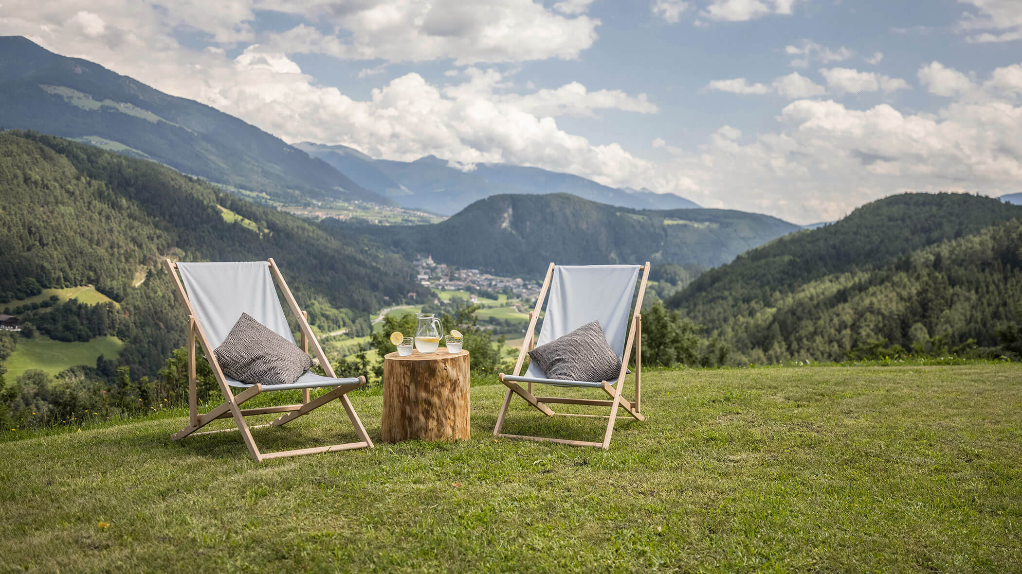 Two deckchairs on a meadow with fresh lemon juice on a tree trunk - Oberplunerhof