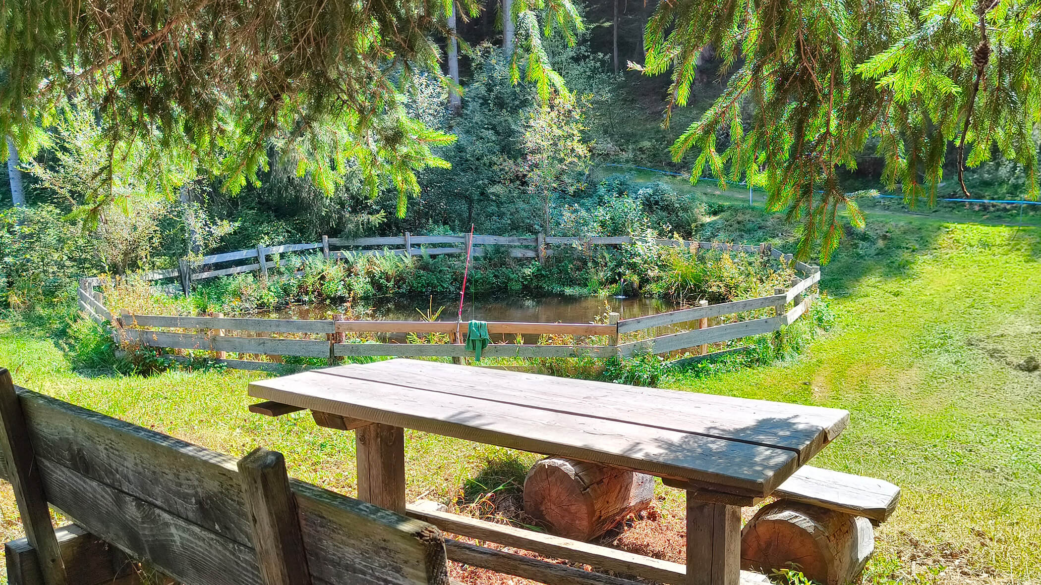 Tavolo e panche di legno davanti a un lago recintato - Oberplunerhof