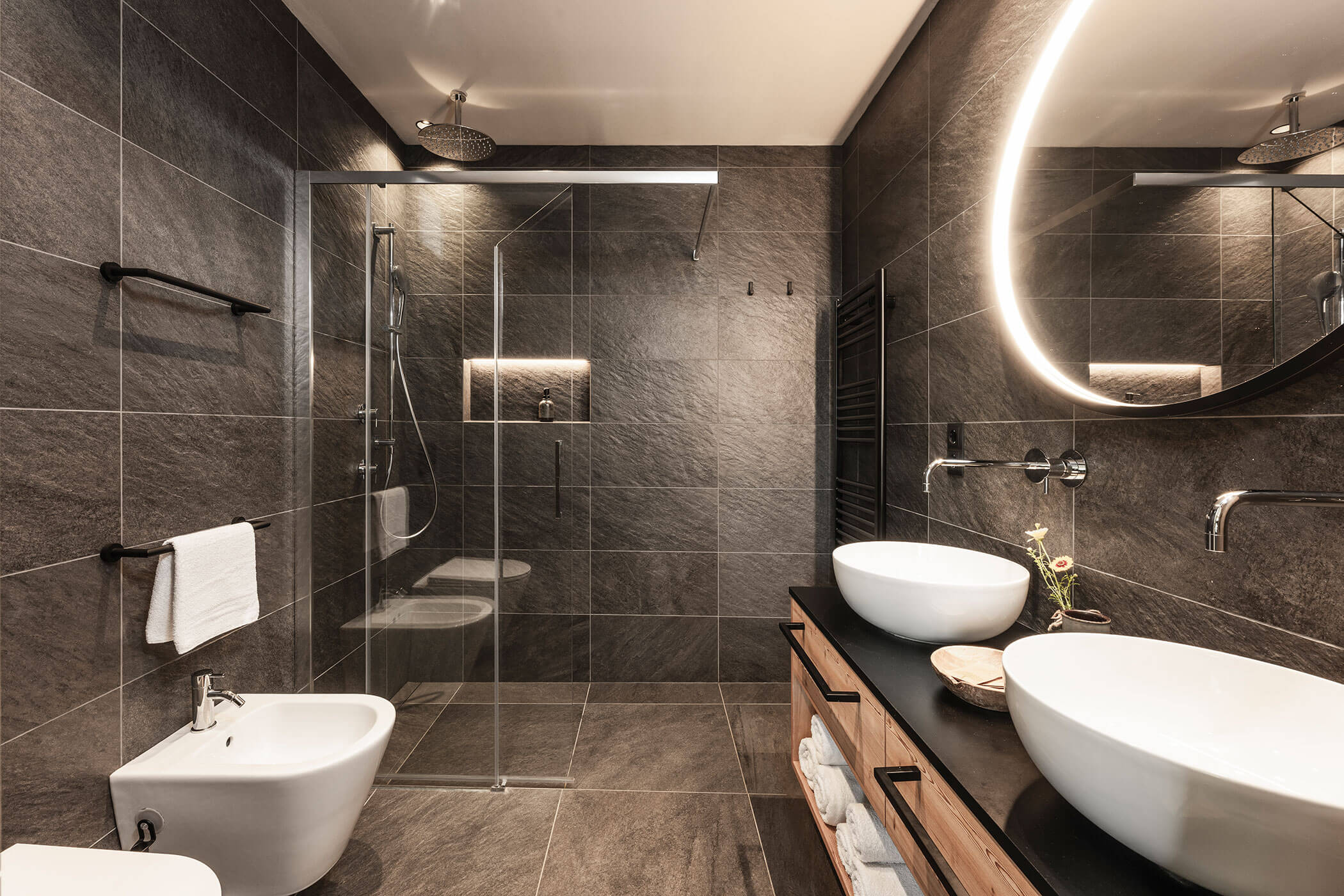 Bathroom in Chalet Woods with large, round mirror, two washbasins, rain shower and WC - Oberplunerhof