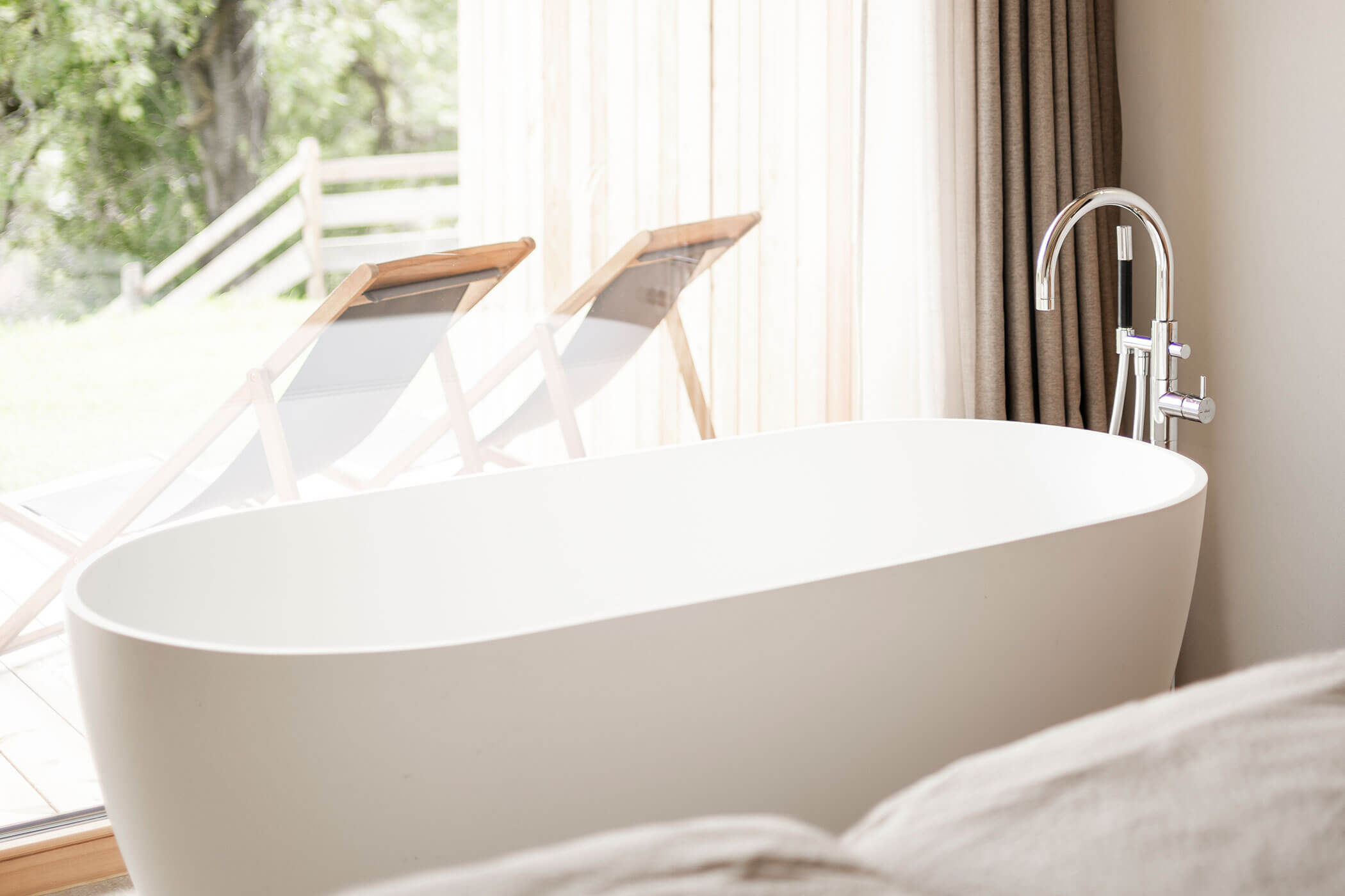 Free-standing bathtub in Chalet Woods with a view of the terrace with two sun loungers - Oberplunerhof