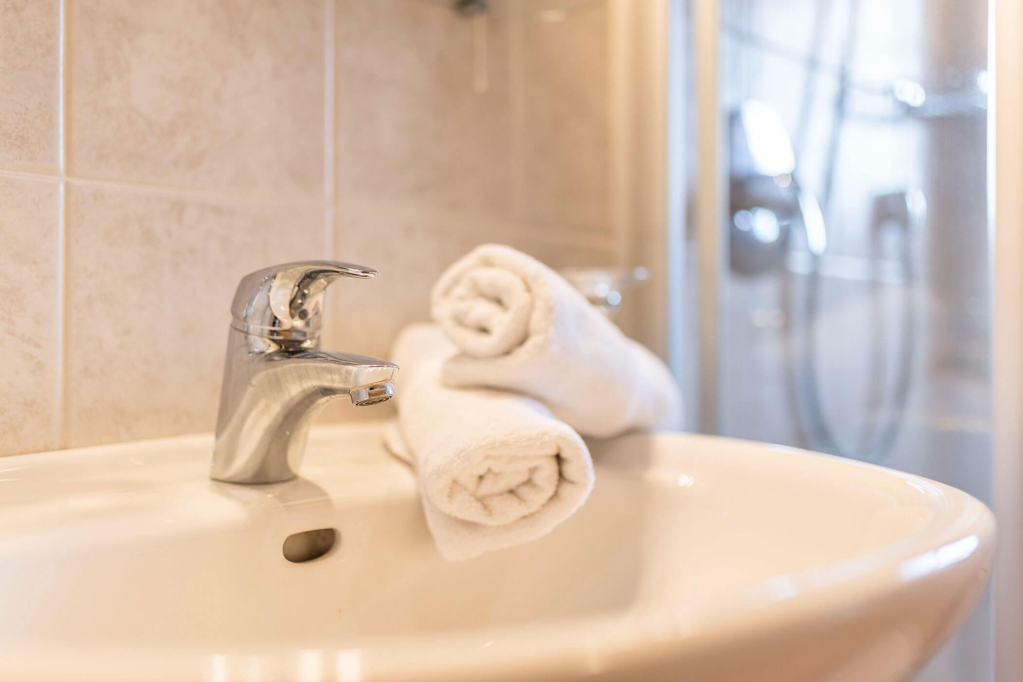 Washbasin with two white towels, a shower in the background - Oberplunerhof
