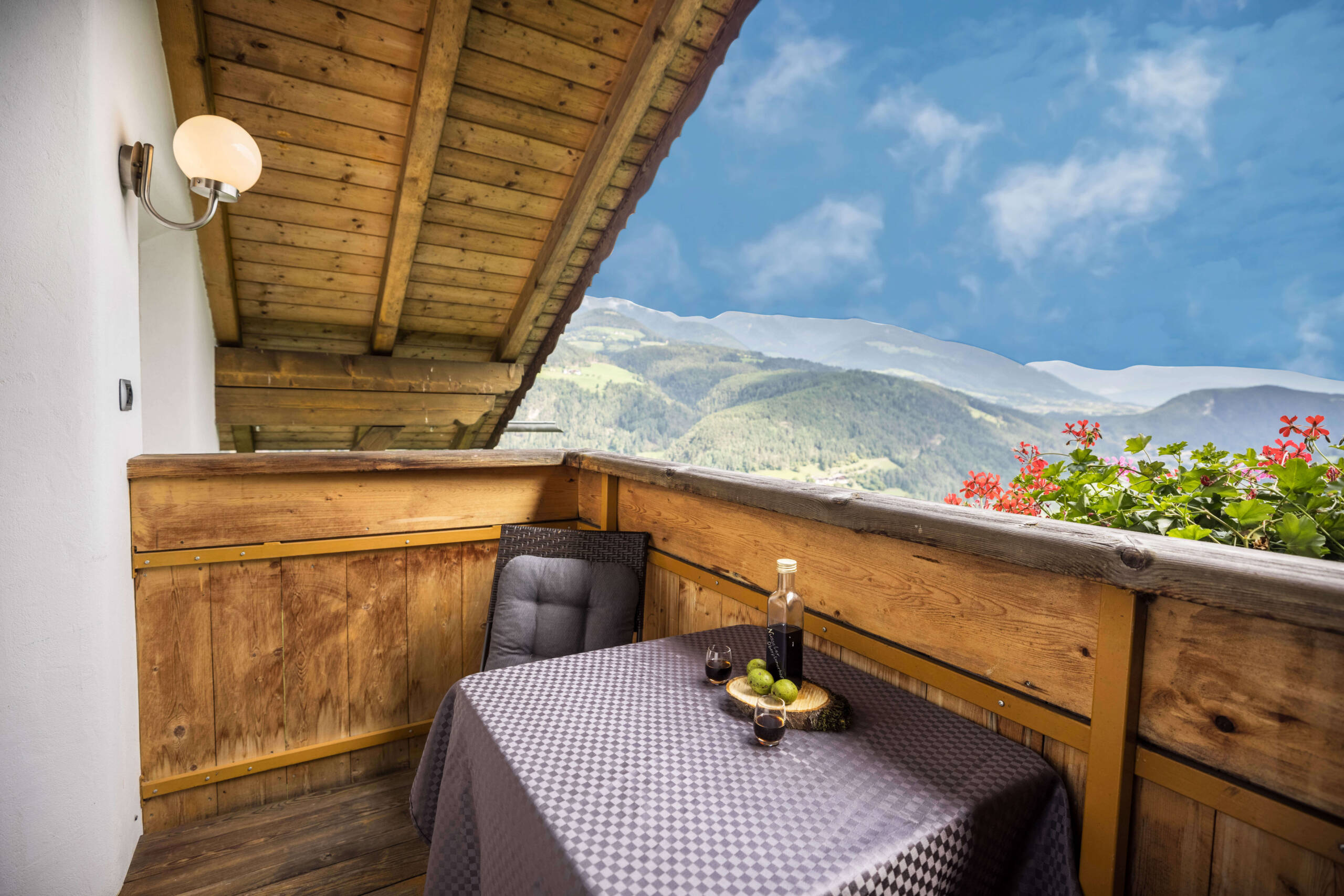 Balcony of apartment Bruenck with a chair and a table, a bottle of wine on it, snow-covered mountains in the background - Oberplunerhof