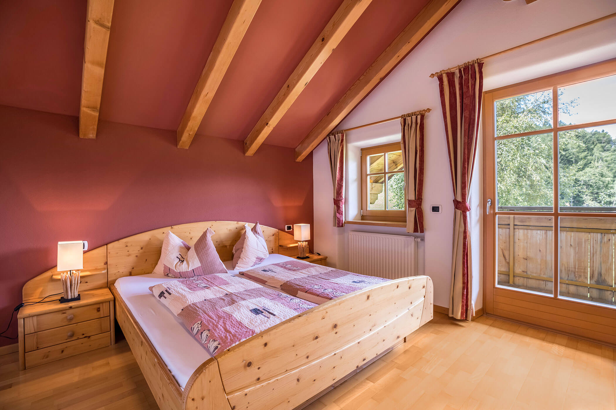 Double bed in the Brunico apartment with bedside lamp and view of the balcony - Oberplunerhof