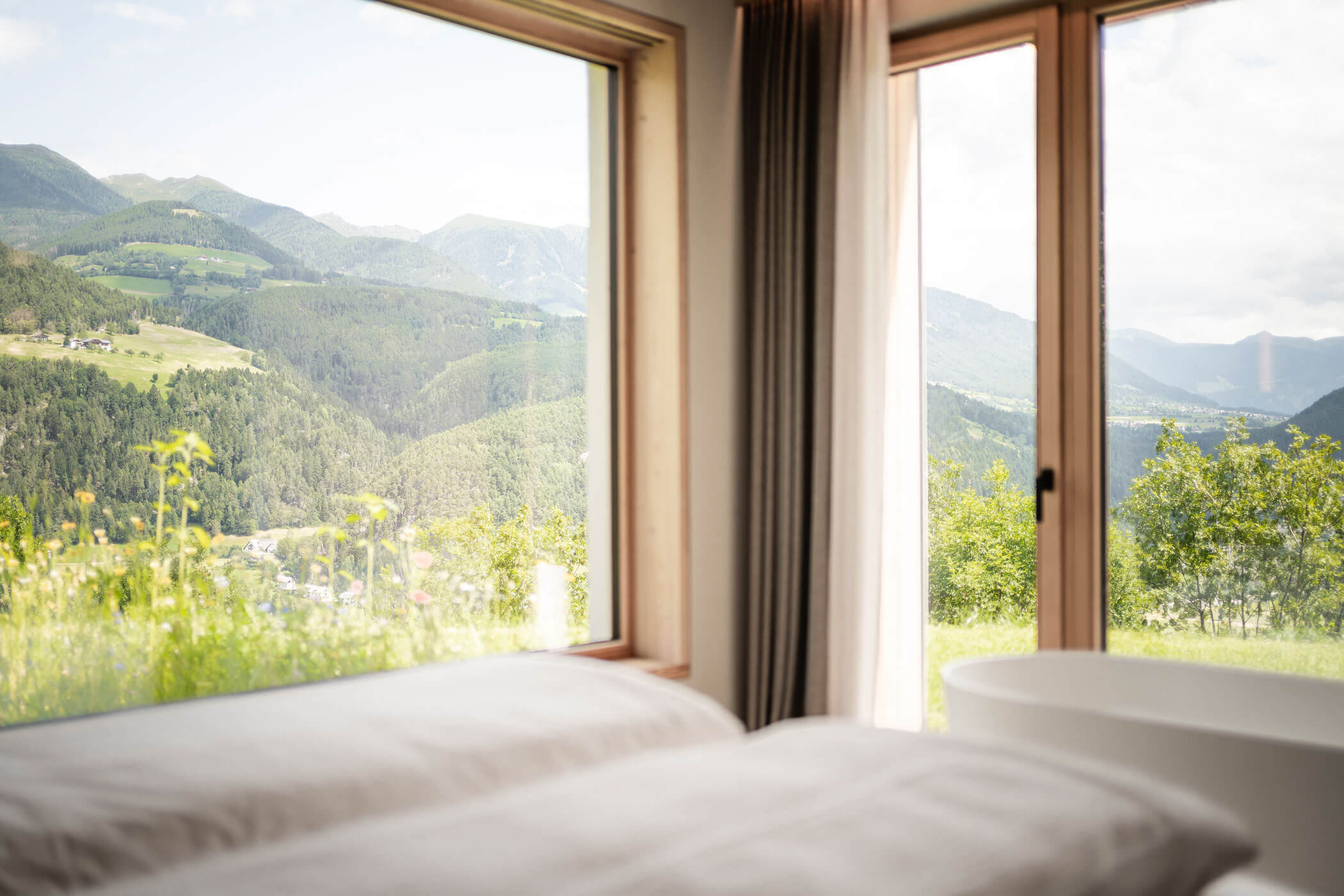 Double bed in Chalet Skyline with free-standing bathtub in front and view of nature - Oberplunerhof